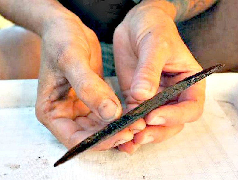Uno de los arqueólogos del equipo científico sostiene entre sus manos un artefacto con dos puntas tallado en madera de 7.000 años de antigüedad. Este artefacto podría haber sido utilizado como anzuelo para capturar peces. (Fotografía: Código Oculto/Angela Dick).