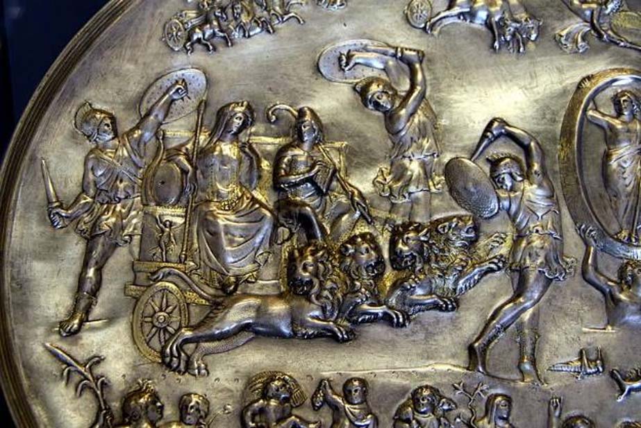 Cibeles y Atis (sentado a la derecha de la diosa, con gorro frigio y cayado de pastor) en un carro tirado por cuatro leones, rodeados de coribantes danzando (detalle de la placa de Parabiago, plata repujada, c. 200 d. C. – 400 d. C., descubierta en Milán, actualmente en el Museo Arqueológico de Milán). (Giovanni Dall’Orto)