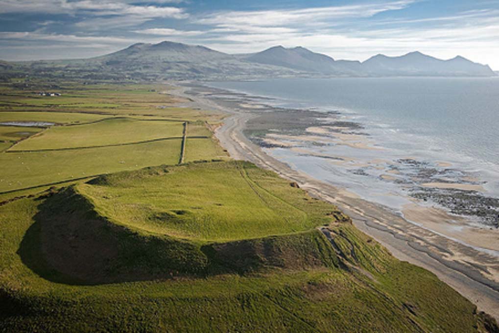 Una fotografÃ­a aÃ©rea del fuerte de la colina de la Edad de Hierro de Dinas Dinlle desde el norte (que sufre erosiÃ³n costera); Gwynedd, Cymru / Gales. Cromlechs y sitios antiguos. (CADW / Visita Gales / CC BY SA 3.0)